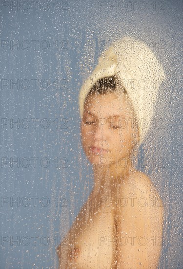 Woman sitting in a steam bath behind glass pane with drops of water, 24 years