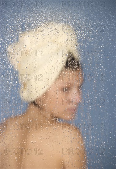 Woman sitting in a steam bath behind glass pane with drops of water, 24 years