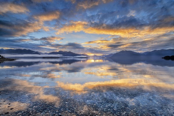 Light beam of golden cloud atmosphere over Lake Te Anau, in the background mountain ranges of the Stuart Mountains and Franklin Mountains