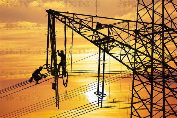 High voltage fitters working on the high voltage pylon at sunset, Baden-Wuerttemberg