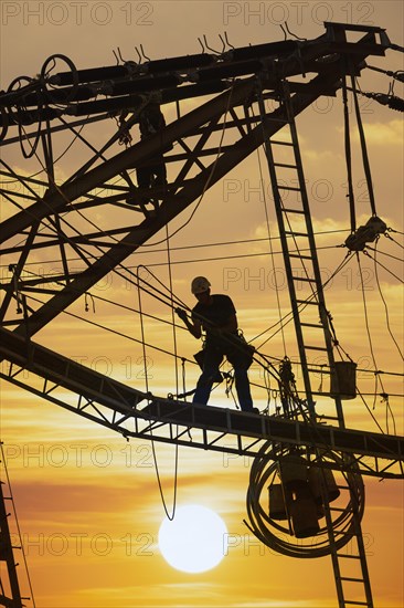 High voltage fitters working on the high voltage pylon at sunset, Baden-Wuerttemberg