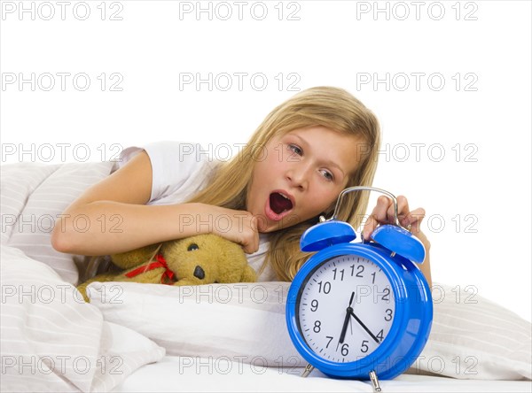 Girl in bed yawns when alarm clock rings