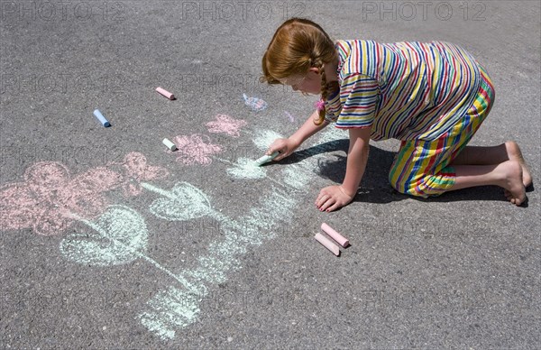 Girl paints flowers with chalk on asphalt