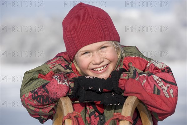 Little girl leaning on a sledge and laughing