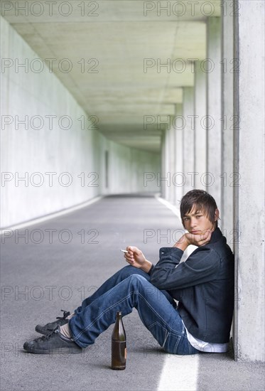 Teenager sitting with beer in an underpass and smoking