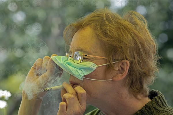 Older woman smoking with a face mask