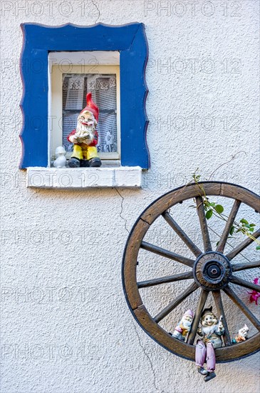 Garden gnomes at a small window and in a wooden wagon wheel