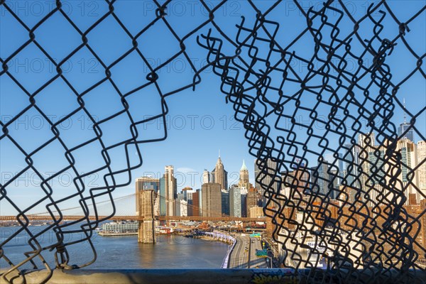 View from Manhattan Bridge through a hole in the wire fence over the East River to the skyline of Lower Manhattan and Brooklyn Bridge