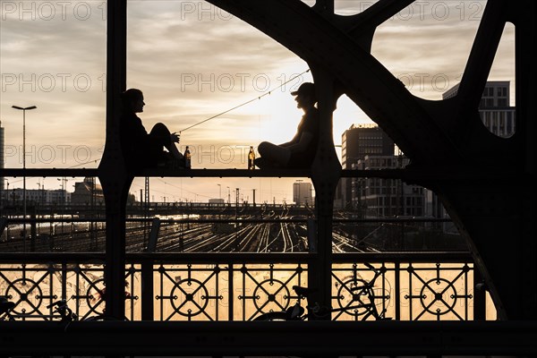 Two people sitting on the parapet and drinking against the light