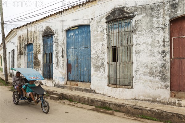 Bicycle taxi driving past decayed facades of crumbling plaster and weathered wooden doors