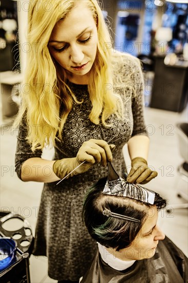 Hairdresser in a hairdressing salon dying strands of hair with aluminium foil