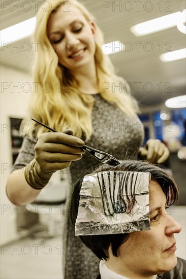 Hairdresser in a hairdressing salon dying strands of hair with aluminium foil