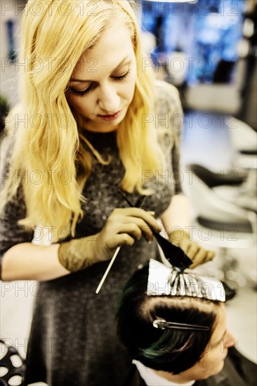 Hairdresser in a hairdressing salon dying strands of hair with aluminium foil