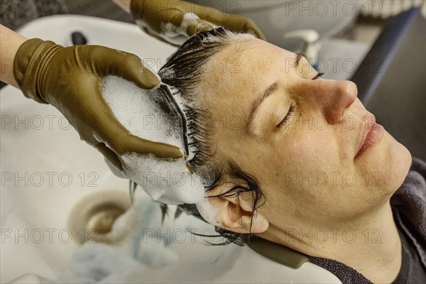 Customer in a hairdressing salon gets her hair washed by a hairdresser with shampoo over a basin