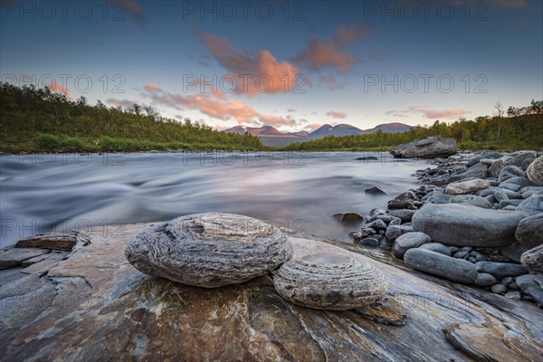 Two round stones lie on the river bank in the evening light