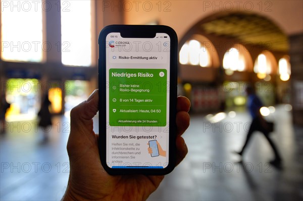 Hand holds smartphone with Corona Warn-APP in the train station