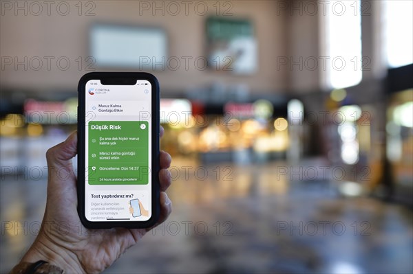 Hand holds smartphone with Corona Warning-APP on TURKISH in the train station