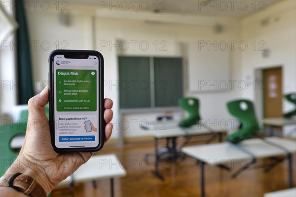 Hand holds smartphone with Corona Warning App in TURKISH in the classroom
