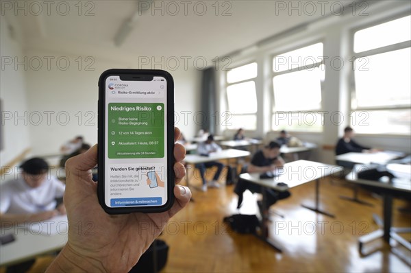 Hand holding smartphone with Corona Warn-APP in a school classroom