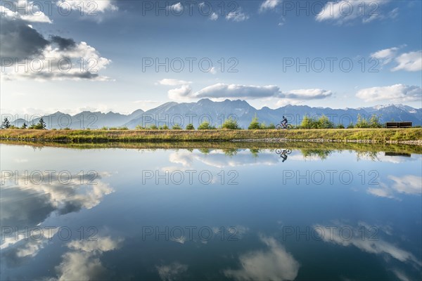 Mountain biker with e-bike on the lakeside in front of a mountain scenery