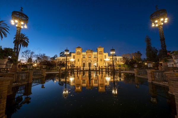 Illuminated art museum Museo de Artes y Costumbres Populares de Sevilla reflected in a fountain