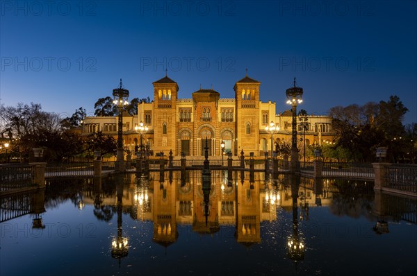 Illuminated art museum Museo de Artes y Costumbres Populares de Sevilla reflected in a fountain