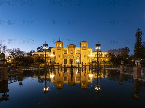 Illuminated art museum Museo de Artes y Costumbres Populares de Sevilla reflected in a fountain
