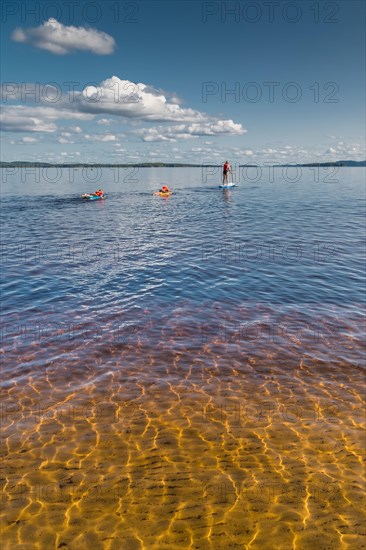 Woman on standup paddling board and children on air mattresses