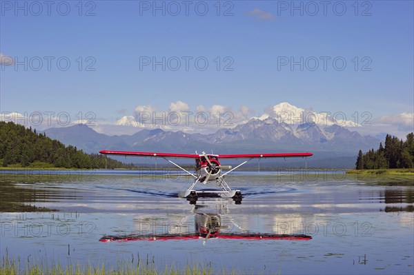 Seaplane Beaver de Havilland lands on a lake off snow-covered mountain Denali