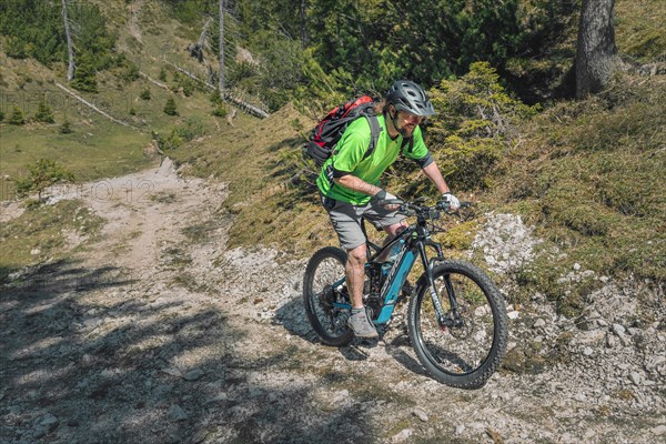 Mountain biker rides with eMTB on a cart track in the mountain forest downhill