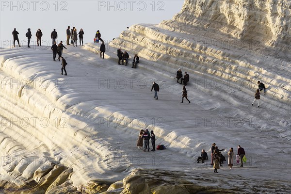 Tourists hiking on chalk cliffs Scala dei Turchi in the evening