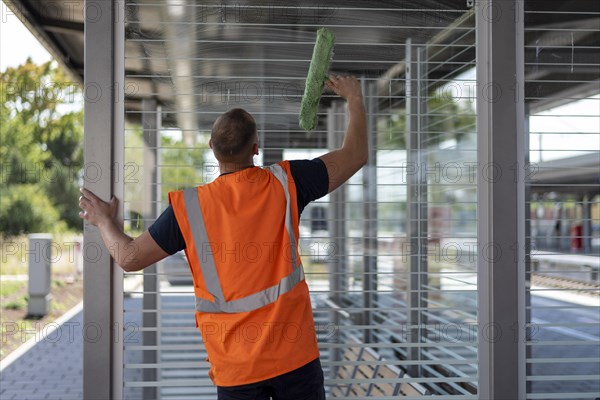 Employee of Deutsche Bahn cleans the glass panes of a waiting area on a platform