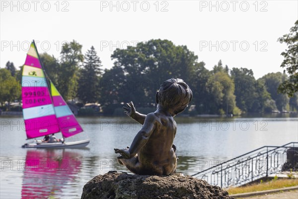 Statue on the beach promenade at Waginger See with sailing boat