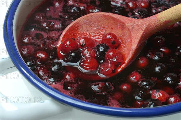 Boiled red and black currants in bowl with wooden spoon