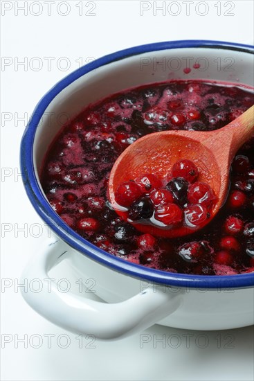 Boiled red and black currants in bowl with wooden spoon