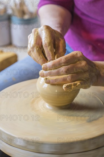 Potter turning a vase with her hands on the potter's pane