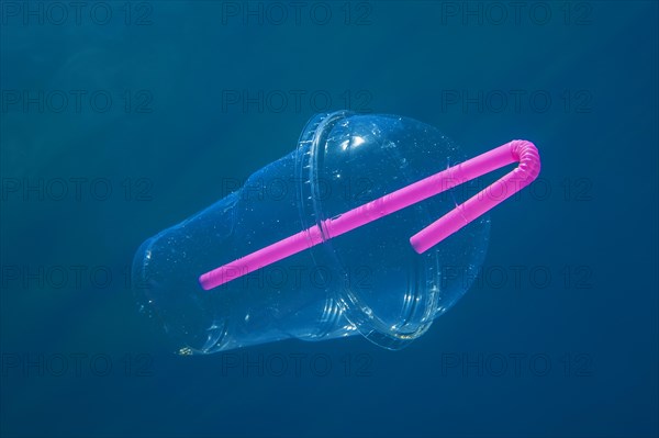 A plastic cocktail cup with a straw floats slowly under water in blue water