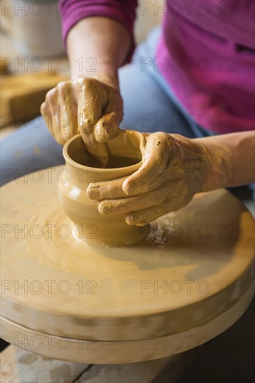 Potter turning a vase with her hands on the potter's pane