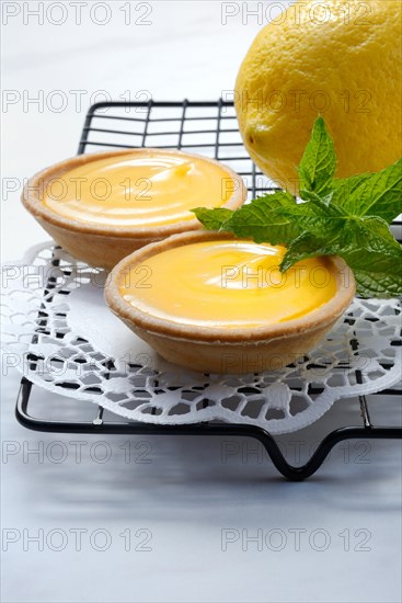 Two lemon tartlets with lemon on a cake rack