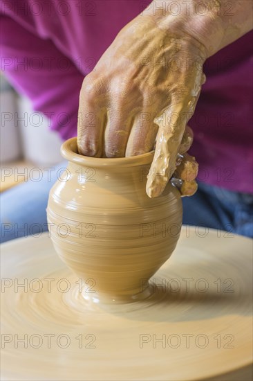 Potter turning a vase with her hands on the potter's pane