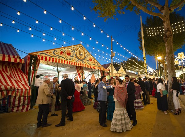 Spaniards celebrating in traditional clothes in front of lit marquees