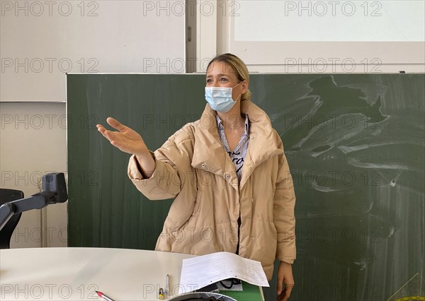 Teacher with thick winter jacket and face mask in classroom teaching
