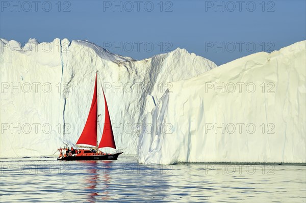 Red sailing boat in front of gigantic icebergs