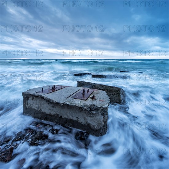 Remains of a bunker in the surf of the Baltic Sea below the steep coast at stormy sea