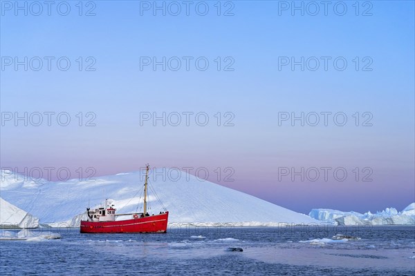 Red boat with tourists in front of icebergs at the blue hour