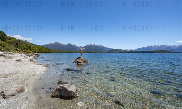 Young man stands on stone in water and stretches his arms in the air