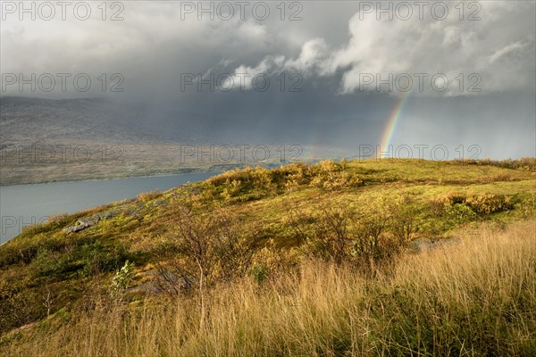 Thunderstorm with double rainbow and dramatic clouds with yellow grass on hills in autumn