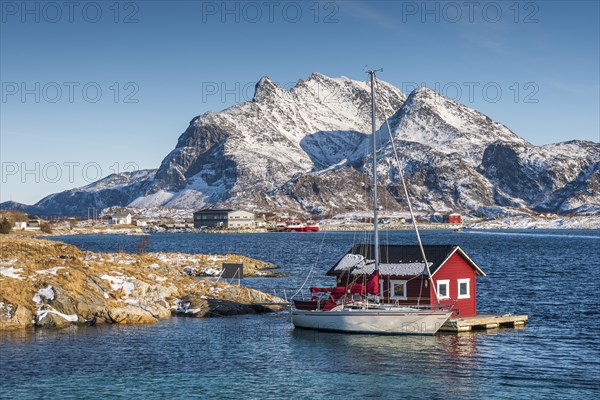 Red wooden cabin on raft with sailing boat in the sea off the coast
