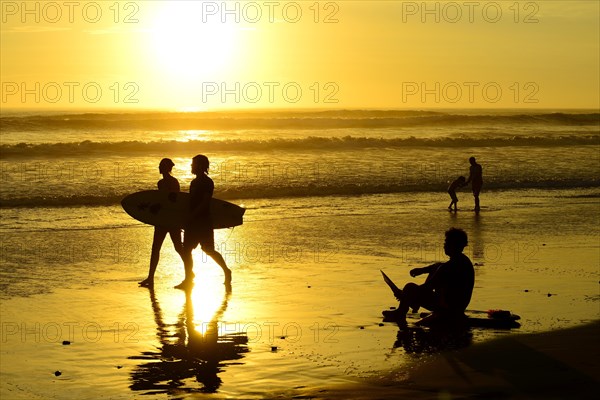 People on the beach with surfboard at sunset