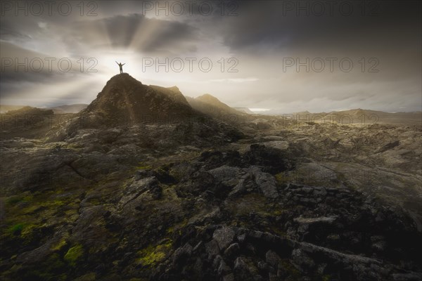 Man on a hill in a black lava field with green moss stretching hands into the dramatic sky